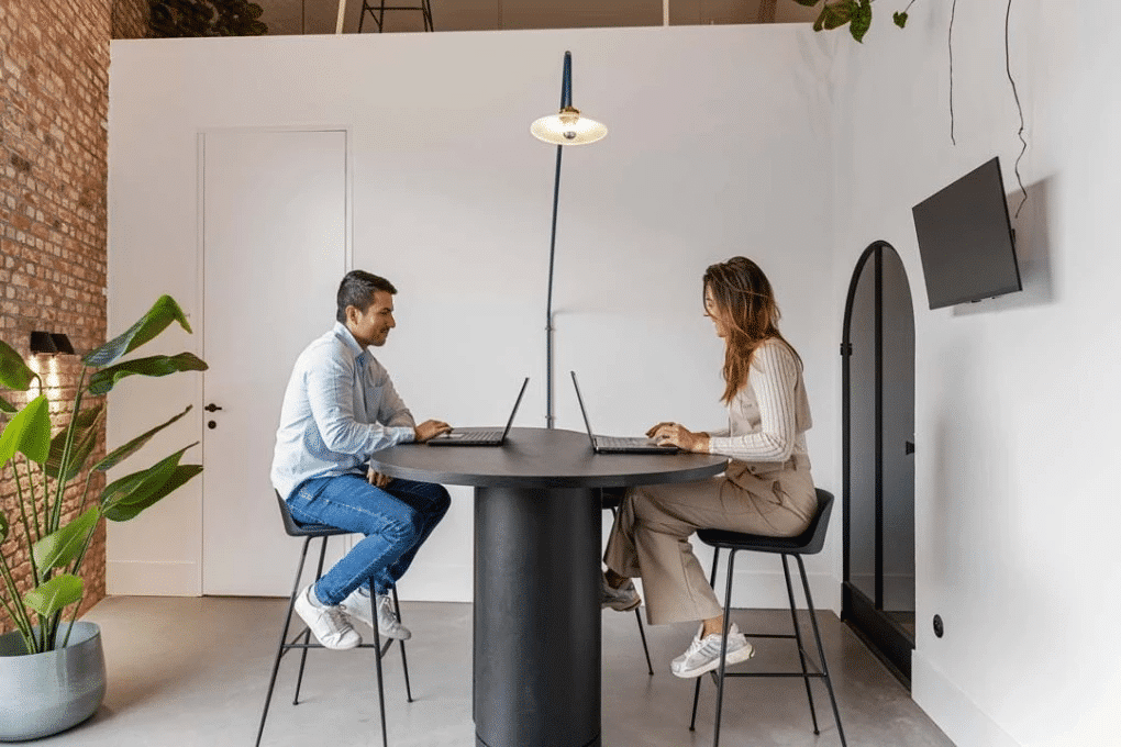 Twee mensen werken aan een hoge tafel in de coworkingruimte van Barn Coworking, ontworpen door Buro Project