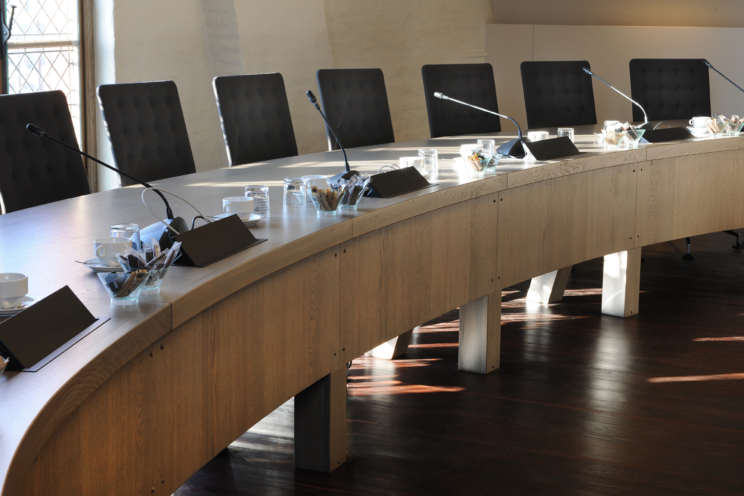 Moderne overleg- en vergaderruimte binnen een overheidsgebouw met gebogen tafel en microfoons